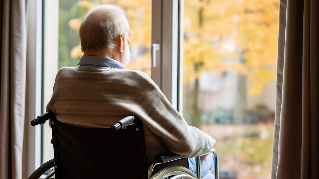 Back view Lonely sad elderly person in wheelchair in home nursing looking out window.