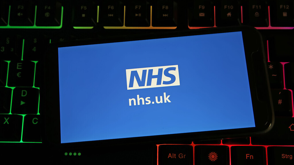 Closeup of mobile phone on computer keyboard with logo lettering NHS.uk national health service