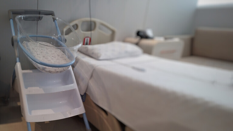 Acrylic crib for newborn, next to the bed in a maternity room.