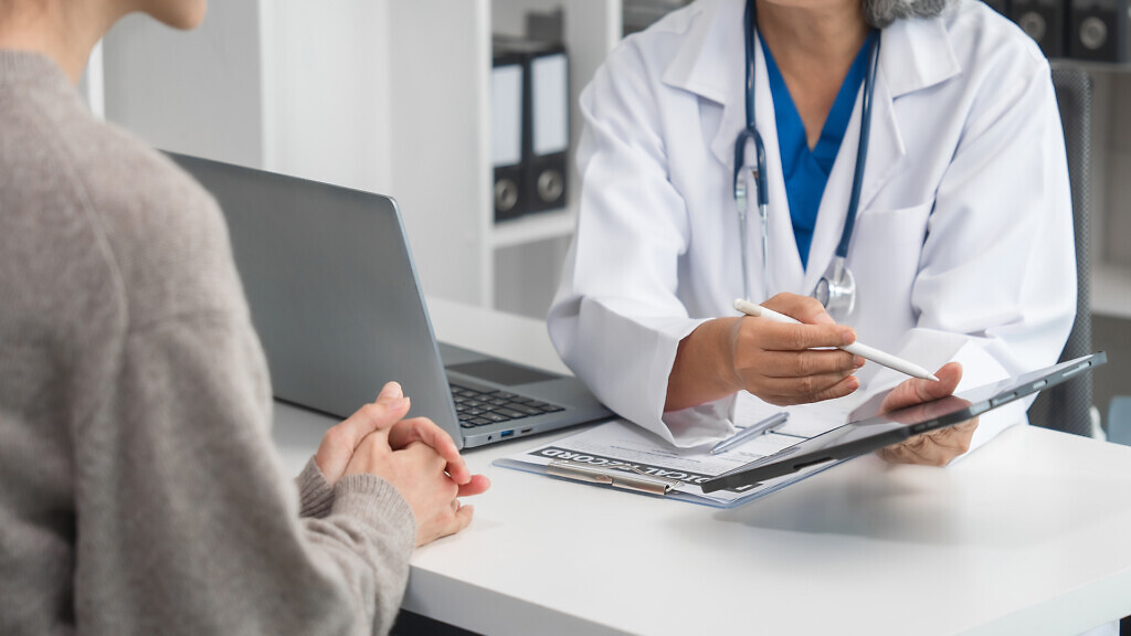 An elderly doctor is talking to a younger Asian woman acro