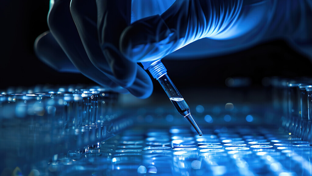 A researcher uses a pipette over test tubes in a lab.