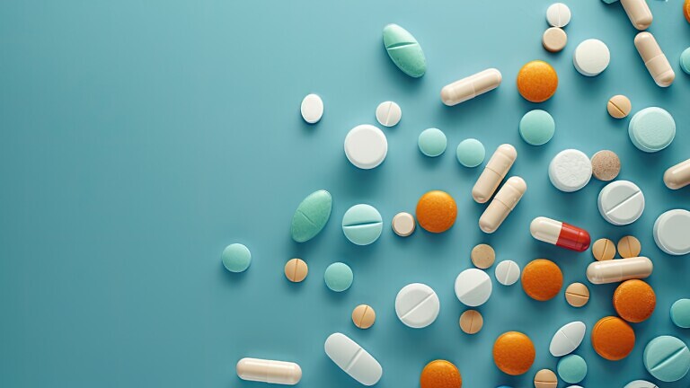 Various drugs like pills, tablets, and capsules arranged on a blue surface seen from above. There is room for text or other elements in the photo. image with copy space