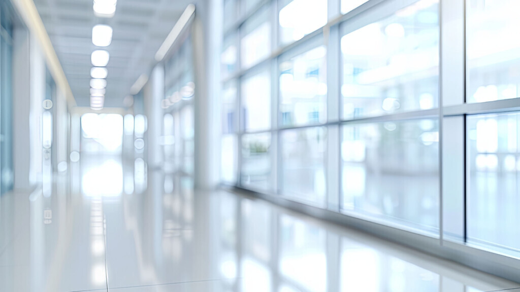 Abstract blurred background of a modern office building hallway with bright windows and white tiled floors.