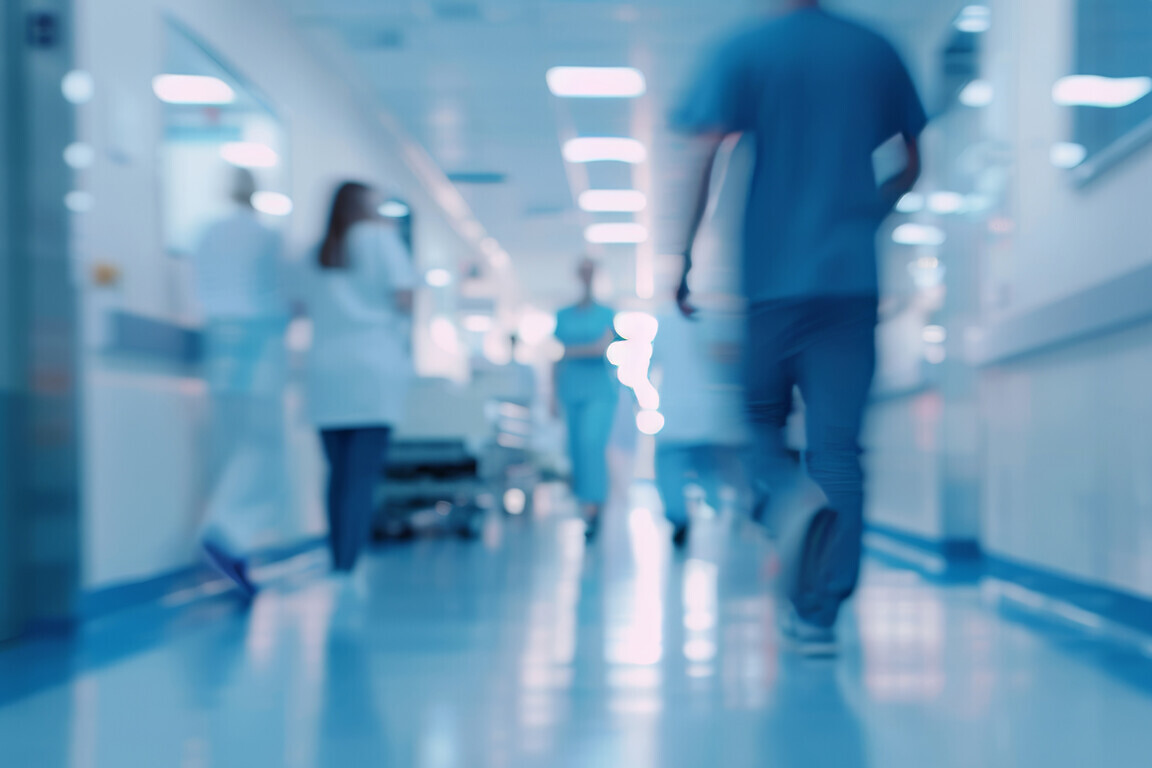 Blurred hospital corridor with people walking and medical staff working in the background.