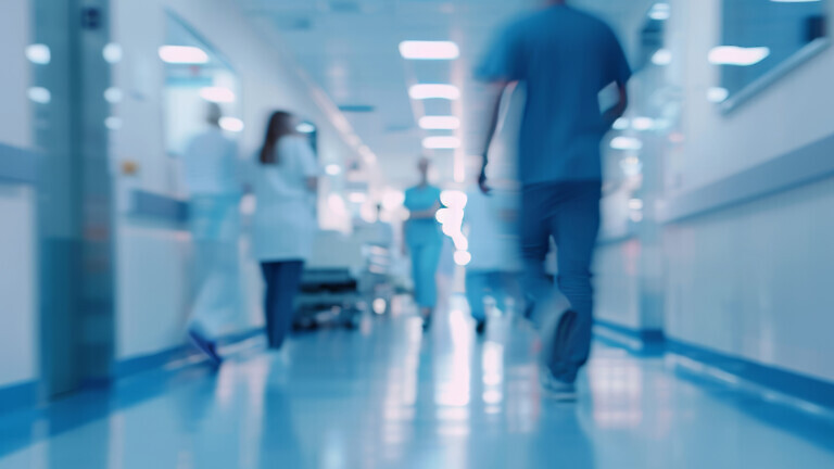 Blurred hospital corridor with people walking and medical staff working in the background.