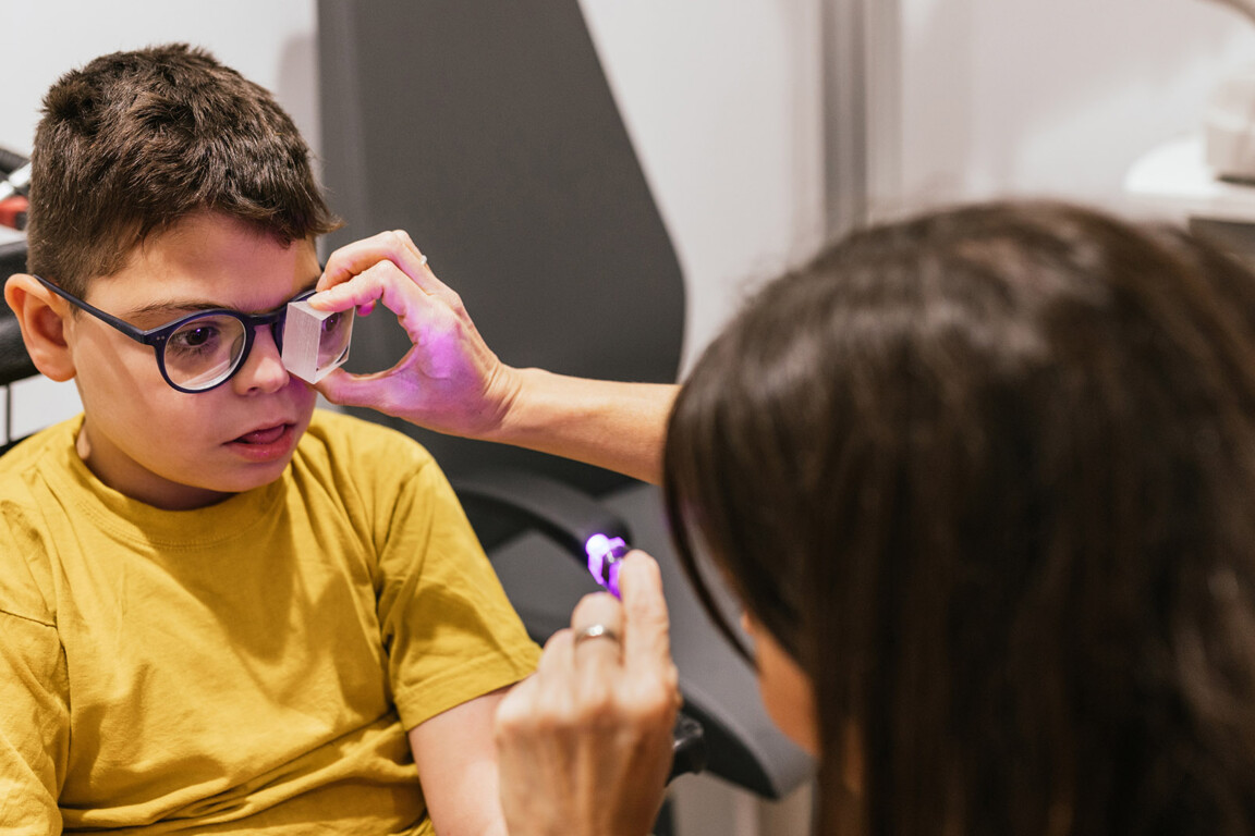Optometrist is performing an eye exam on a young boy with cerebral palsy, using specialized equipment to assess his vision