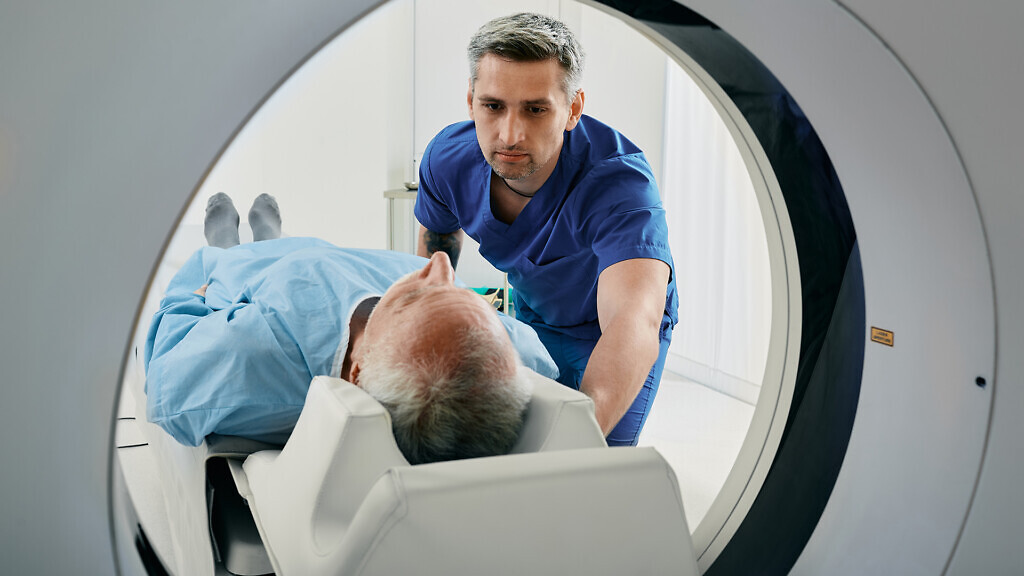 Senior man going into CT scanner. CT scan technologist overlooking patient in Computed Tomography scanner during preparation for procedure