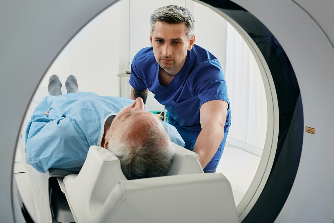 Senior man going into CT scanner. CT scan technologist overlooking patient in Computed Tomography scanner during preparation for procedure