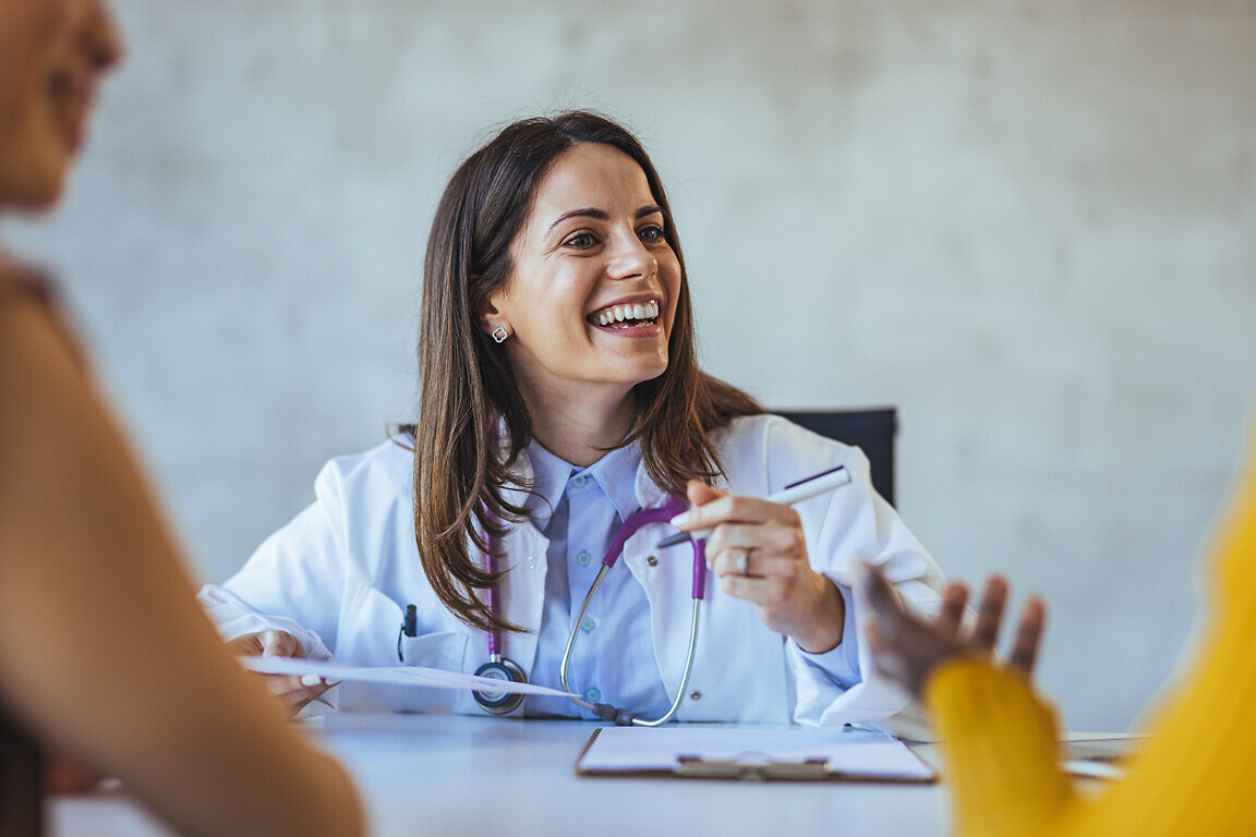 A smiling female doctor engages with her patients in a bright office setting, creating a warm and welcoming atmosphere during a medical consultation.