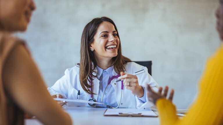 A smiling female doctor engages with her patients in a bright office setting, creating a warm and welcoming atmosphere during a medical consultation.